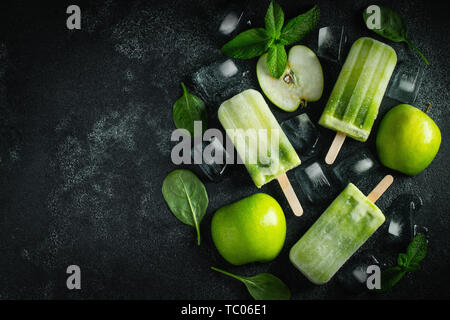Bright popsicle made of green apple and fresh mint on a dark concrete background. Sweet summer treat. Top view with copy space. Flat lay. Stock Photo