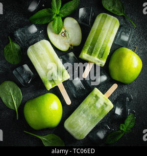 Bright popsicle made of green apple and fresh mint on a dark concrete background. Sweet summer treat. Top view. Flat lay. Stock Photo