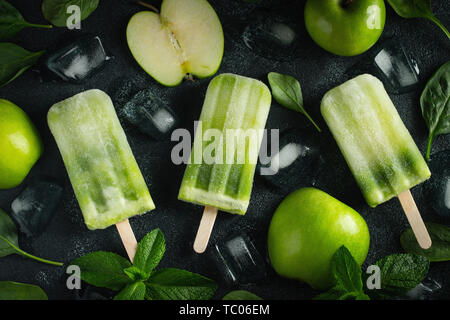 Bright popsicle made of green apple and fresh mint on a dark concrete background. Sweet summer treat. Top view. Flat lay. Stock Photo