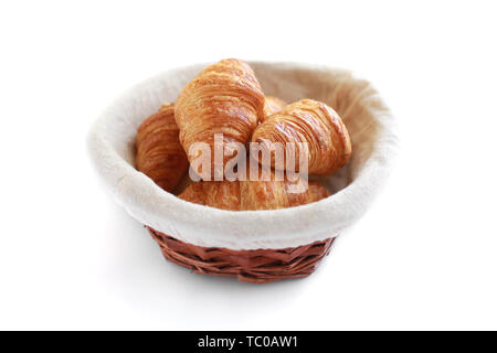 Five freshly baked tasty crusty croissants in wicker basket isolated on white. Stock Photo