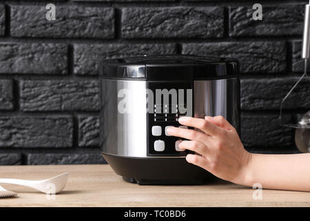 Woman switching on modern multi cooker on table Stock Photo