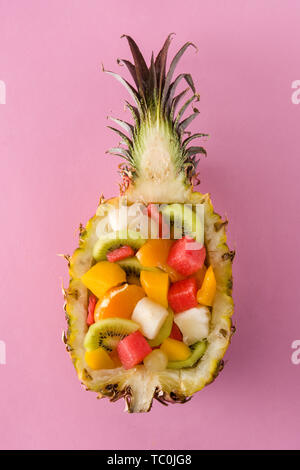 Mix fruit served inside pineapple on pink background Stock Photo