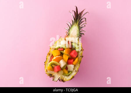 Mix fruit served inside pineapple on pink background Stock Photo