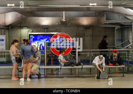 People sit on a bench on the platform at Westminster London Underground Station Stock Photo