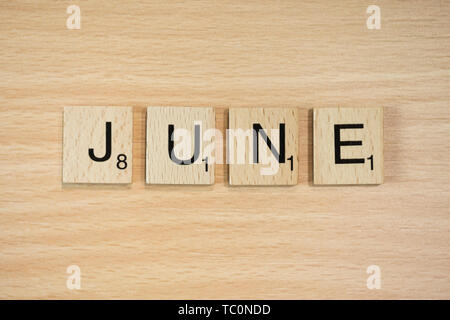 The word March, spelt out using wooden tiles on a wood effect background with scrabble numbered score values. Stock Photo