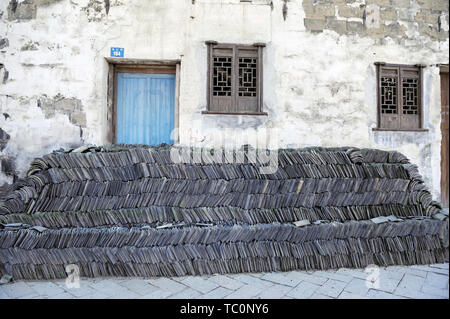 Stacked black roof tiles against a wall of a house that is renovated in Tongli, China Stock Photo