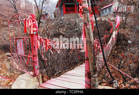 In front of the temple in the mountains, there is a suspension bridge full of red ropes for blessings. Stock Photo