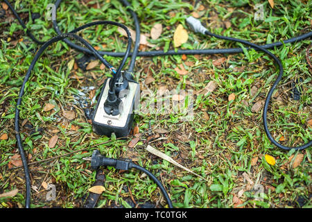 socket, plug and electric black cable on the grass in the garden. Stock Photo