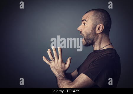 Studio portrait of man with short hair and surprised expression beard and hands folded ahead of him. Seen in profile. Stock Photo