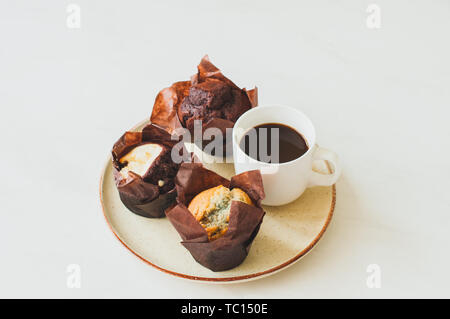 A cup of coffee and three muffins on a plate on a white bacground. Close up. Stock Photo