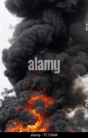 View of huge flames of red-orange fire and motion clouds of black smoke covered sky. Selective focus, motion blur from strong fire and high temperatur Stock Photo