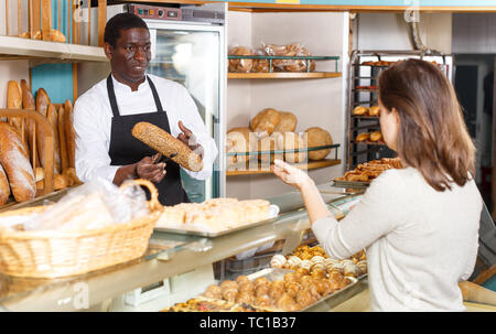 Polite male baker working behind counter in store of his bakery, serving female customer Stock Photo