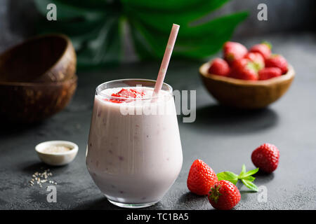 Strawberry coconut smoothie or milkshake in glass with drinking straw on black background Stock Photo