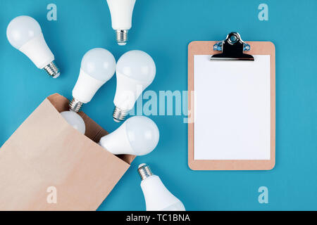 Energy-saving and eco-friendly life in conceptual composition. Creative top view flat lay of LED light bulbs in craft paper shopping bag and clipboard Stock Photo