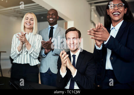 Smiling group of diverse businesspeople clapping while watching a presentation together in an office Stock Photo