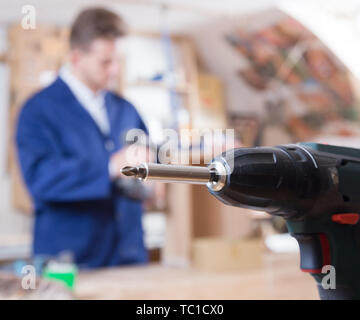 Young smiling guy using drilling machine at workshop Stock Photo