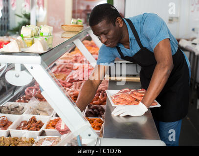 Professional butcher arranging meat products in display case of butcher shop Stock Photo