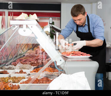 Professional butcher arranging meat products in display case of butcher shop Stock Photo