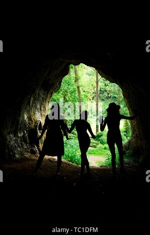 Dark female silhouettes at the entrance to natural cave in the forrest Stock Photo