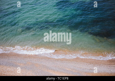 Clear blue water with waves washing the sandy shore. Top view, background. Sea or an ocean Stock Photo
