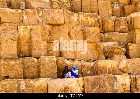 Photo: © Simon Grosset. The Giza Pyramid complex, or Giza Necropolis, near cairo, Egypt. A couple rest in the shade on the blocks of the Great Pyramid Stock Photo