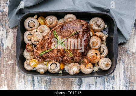 Marinated lamb with mushrooms, spices and herbs in a cast-iron mold on a wooden background. Halal meat and food. Top view Stock Photo
