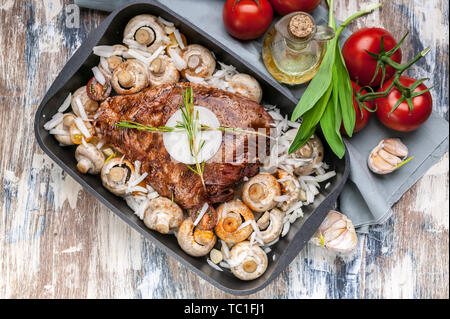 Marinated lamb with mushrooms, spices and herbs in a cast-iron mold on a wooden background. Tomatoes and olive oil. Halal meat and food. Top view Stock Photo