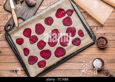 Baking sheet with tasty raw beet chips on wooden table Stock Photo