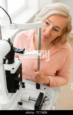 Holding metal tubes . Focused woman looking on her doctor while sitting in front of apparatus and checking her eyesight Stock Photo