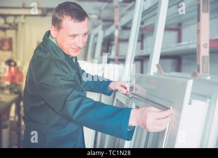 Smiling production young worker in coverall with different PVC windows and doors Stock Photo