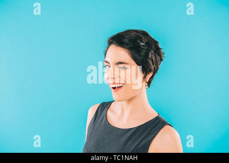 cheerful mixed race woman winking at camera isolated on blue Stock Photo