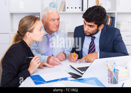 Managers are writing financial reports and discussing with mature boss in the office. Stock Photo