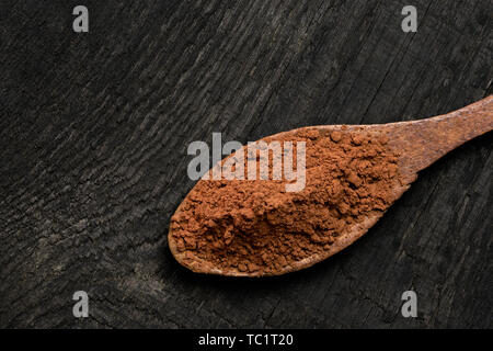 Cocoa powder on a wooden spoon isolated on black rustic wood board from above. Space for text. Stock Photo