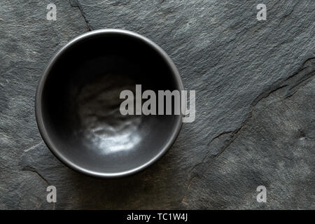 Black empty ceramic bowl isolated on dark grey slate from above. Space for text. Stock Photo