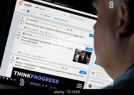 Man sitting at a computer monitor browsing through the Internet looking at the Reddit website on the World Wide Web using an Internet Browser. Stock Photo
