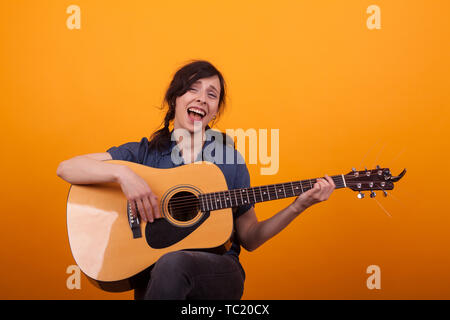 Portrait young singer with acustic guitar in studio over yellow background. Cheerul young artist with her guitar. Stock Photo