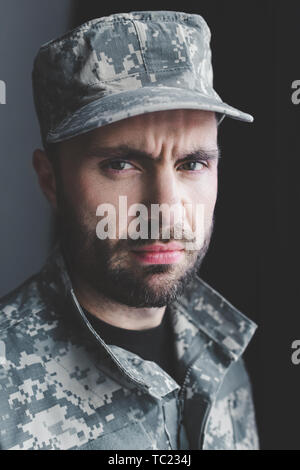 Bearded military man looking at camera with serious face against brick