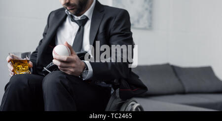 panoramic shot of disabled man in wheelchair holding ball and glass of whiskey Stock Photo