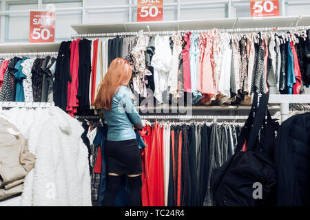 red hair young girl in blue leather jacket chooses clothes in store. woman shopaholic makes a purchase in the supermarket Stock Photo