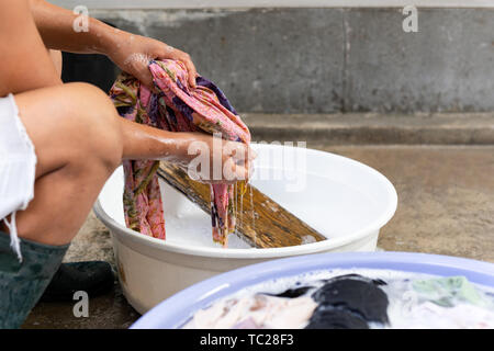 Woman hands washing dirty clothes in big bowl on concrete floor Stock Photo