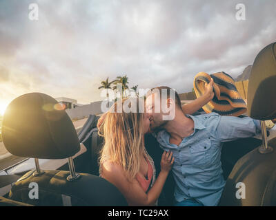Happy young couple having kissing in convertible car during their road trip - Trendy romantic lovers having a tender moment in cabriolet auto