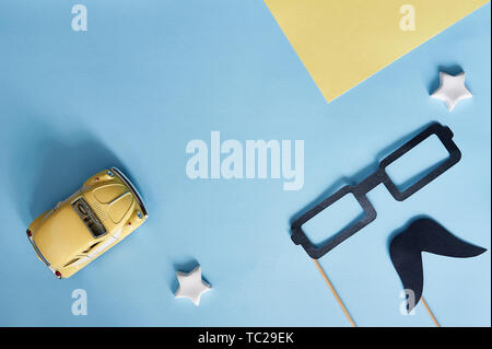 Kiiv, Ukraine - June 6, 2019: Happy Father's Day top view. Decorative black paper mustache, glasses and yellow toy car on a blue background with place Stock Photo