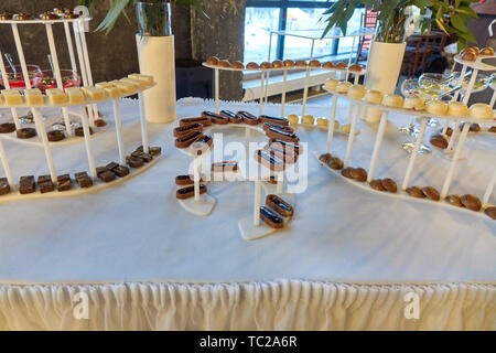 Candy bar on the white table with a different kunds of sweets and other desserts beautiffully served on the wedding Stock Photo