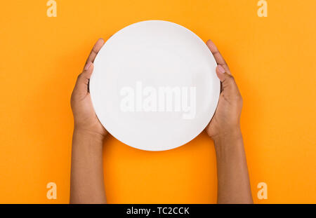 Female hands holding empty plate on orange background Stock Photo