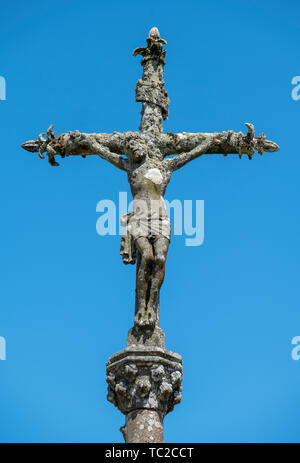 Stone statue of Christ on the cross against a blue sky at a cemetery in La Feuillée, Brittany, France. Stock Photo
