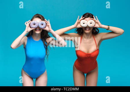 two girls in swimsuits holding donuts isolated on blue Stock Photo