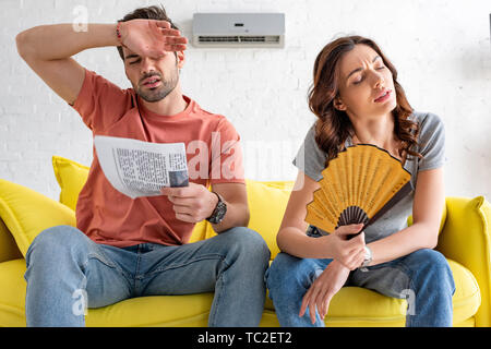exhausted man and woman sitting on sofa and suffering from heat at home Stock Photo