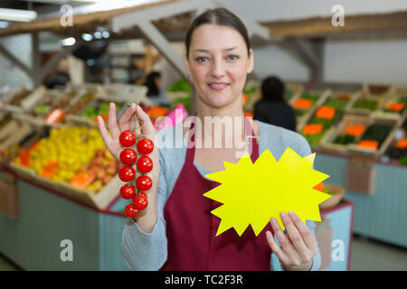 female grocer holding vine tomates and blank promotional card Stock Photo