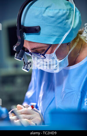 Close up portrait of female surgeon doctor wearing protective mask and hat during the operation. Healthcare, medical education, surgery concept. Stock Photo