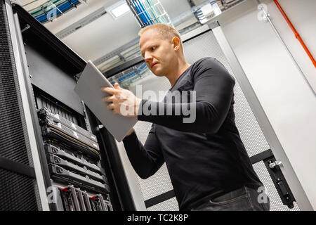 Male Technician Using Digital Tablet In Datacenter to Monitor SAN and Servers Stock Photo
